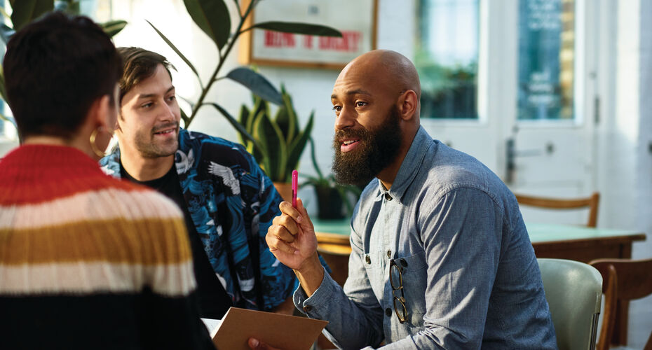 Three men engaged in a conversation while seated around a table.