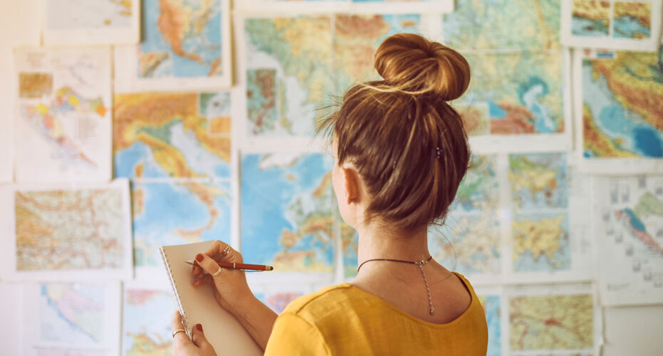 Young woman handwriting at notebook while looking at map