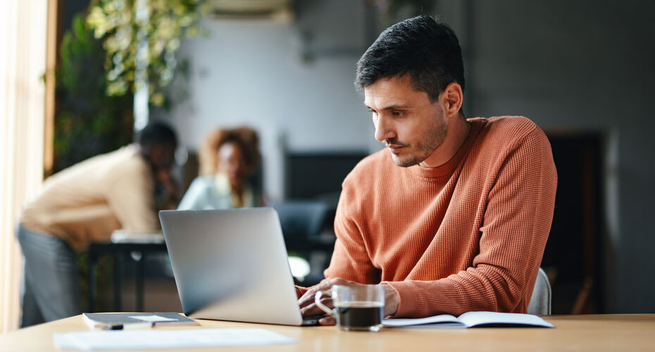 A serious man typing on his laptop while sitting at the office desk